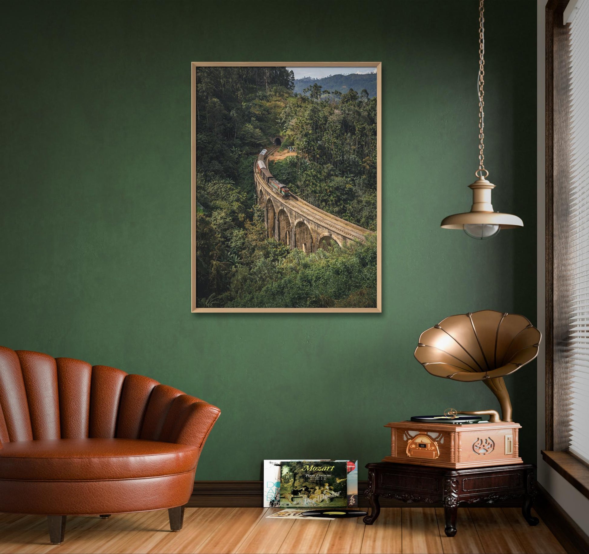 Une chambre confortable dispose d'un fauteuil vintage, d'un gramophone et d'une pile de disques. Sur le mur végétal, une photographie encadrée Fine Art Shots intitulée "Un billet pour le passé" (Sri Lanka) représente le chef-d'œuvre de l'ingénierie du Sri Lanka, le pont aux neuf arches, niché dans un écrin de verdure. Une suspension ronde est suspendue au plafond.