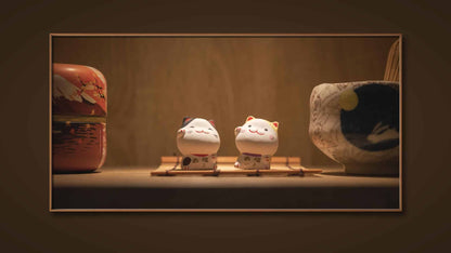 Une photographie encadrée représentant deux figurines de chats en céramique "Les chats porte-bonheur" (Taïwan) aux visages souriants assis sur des plates-formes en bois. Ils sont entourés de poteries japonaises traditionnelles, dont un bol à thé et un récipient au design scénique, le tout sur un fond chaleureux en bois. Cette belle pièce vous est présentée par Fine Art Shots.